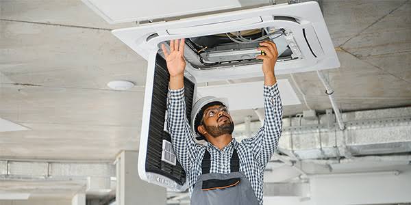 Technician servicing a ceiling-mounted HVAC cassette system