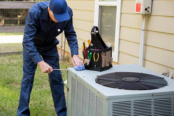 Technician performing seasonal maintenance on an outdoor air conditioning condenser